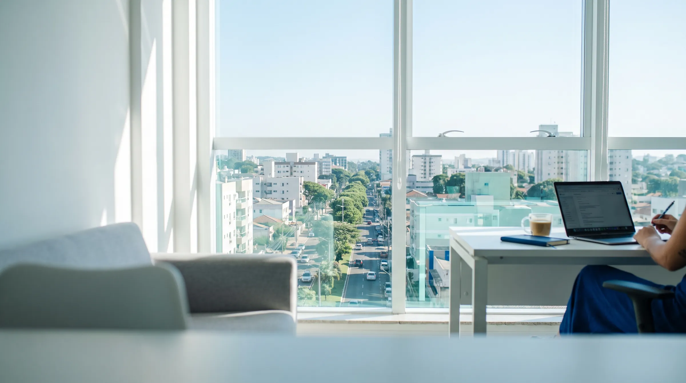 Escritório claro com notebook e janelas com vista para a cidade