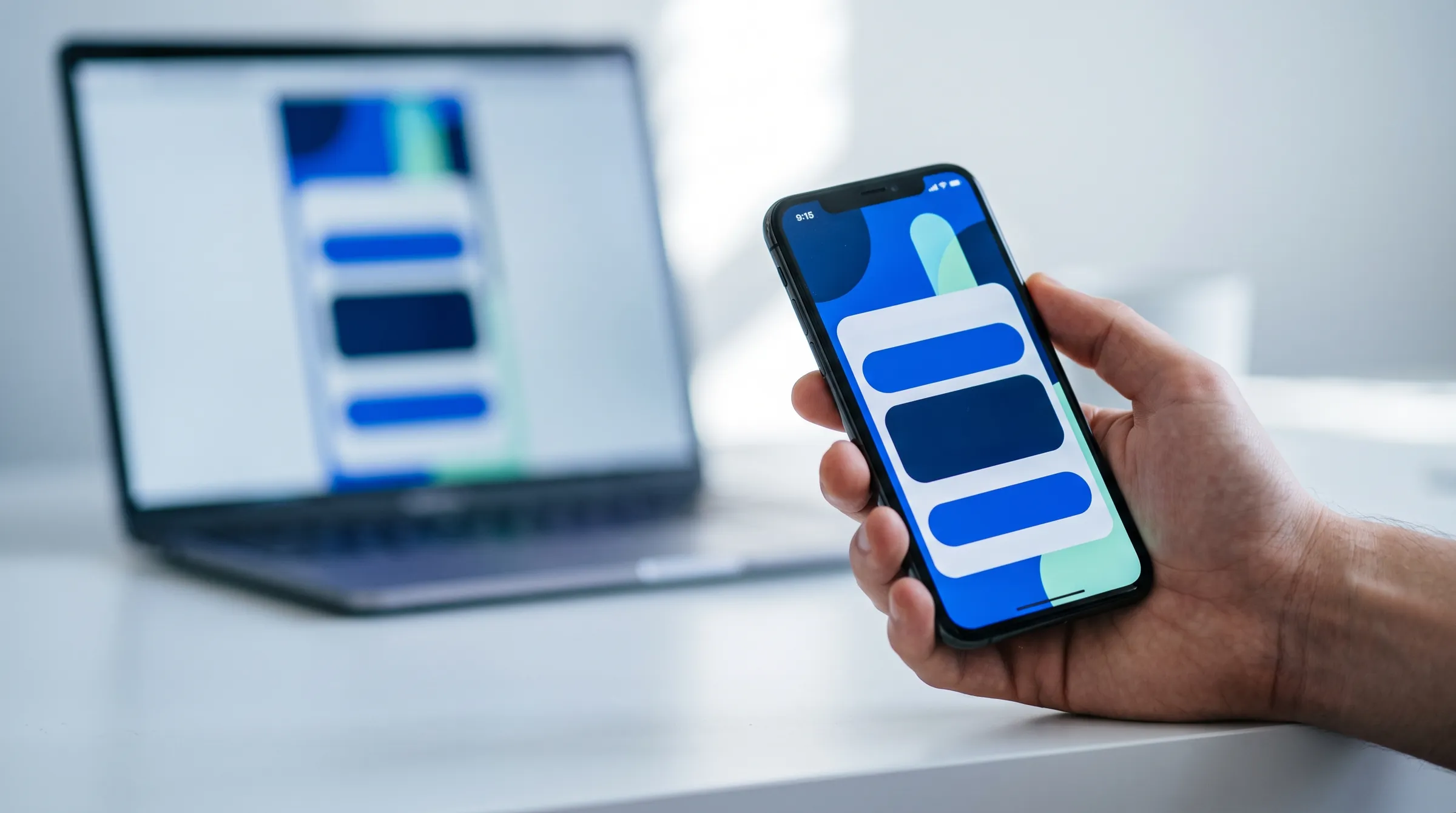 Mão segurando um celular com um formulário de uma página, com o notebook ao fundo