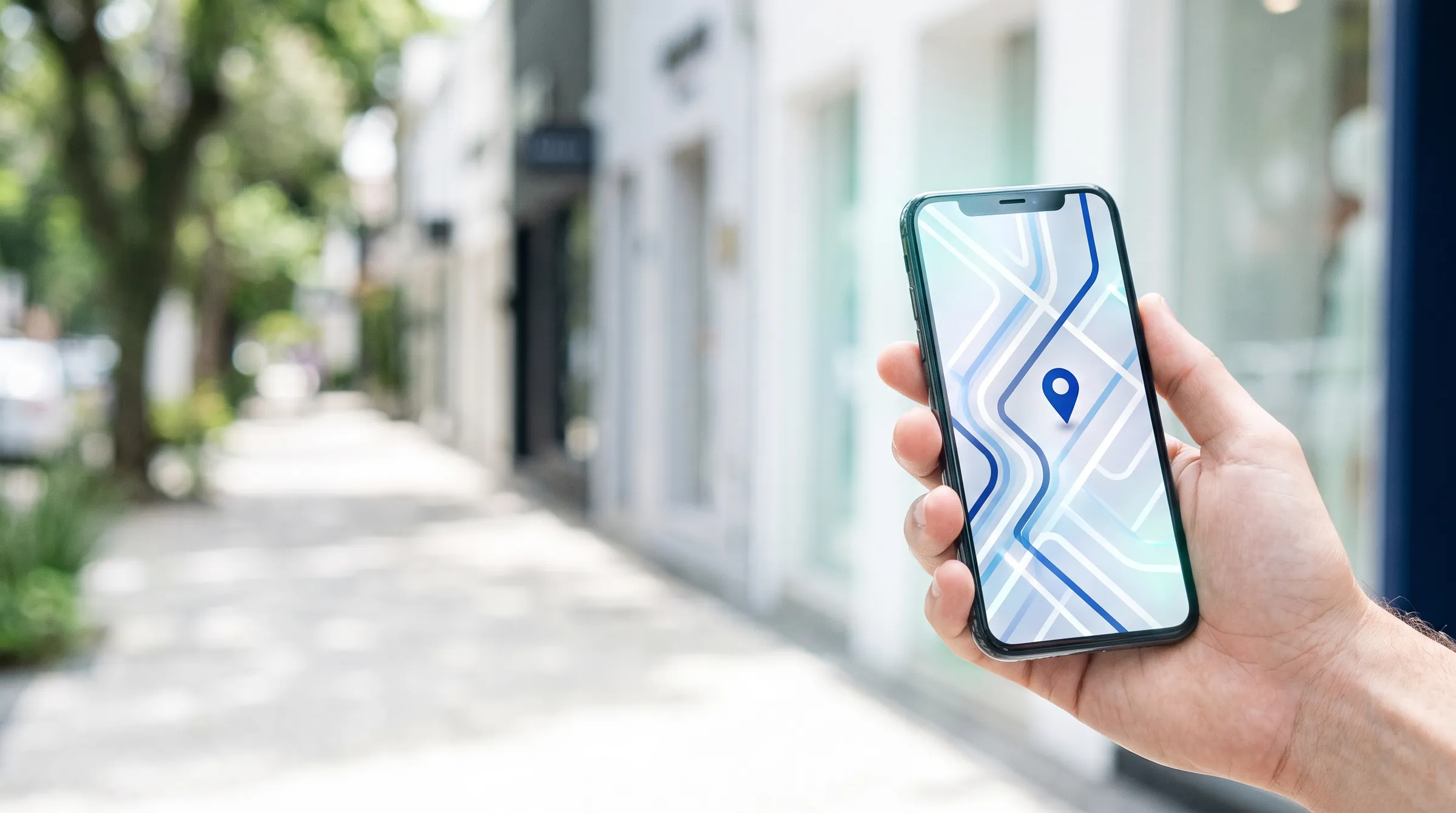 Mão segurando um celular com um mapa e um marcador azul em uma rua arborizada